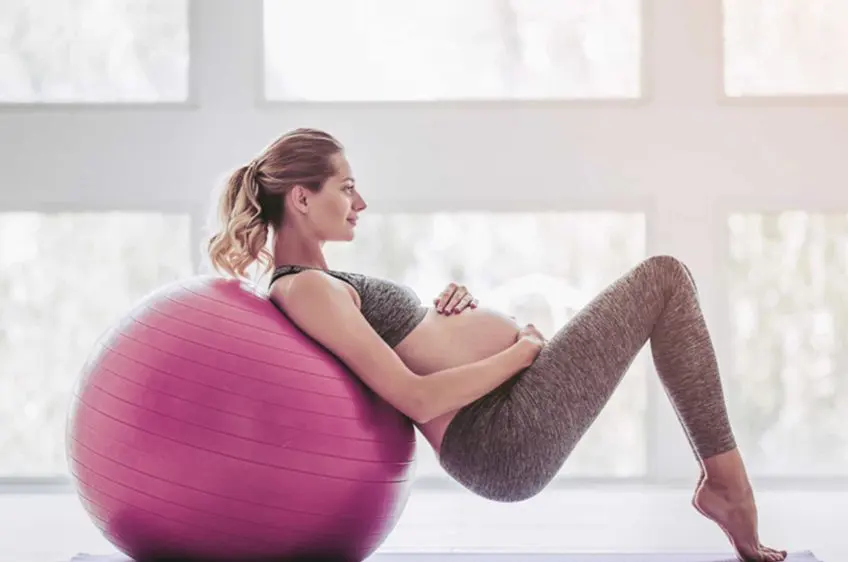 Grávida a fazer um exercício de Pilates, deitada para trás sobre uma bola