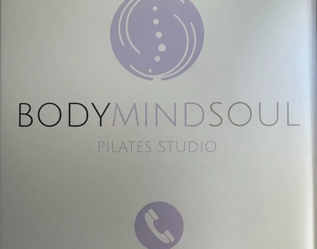 Placa do BodyMindSoul à entrada do estúdio, com o logótipo e os números de telefone